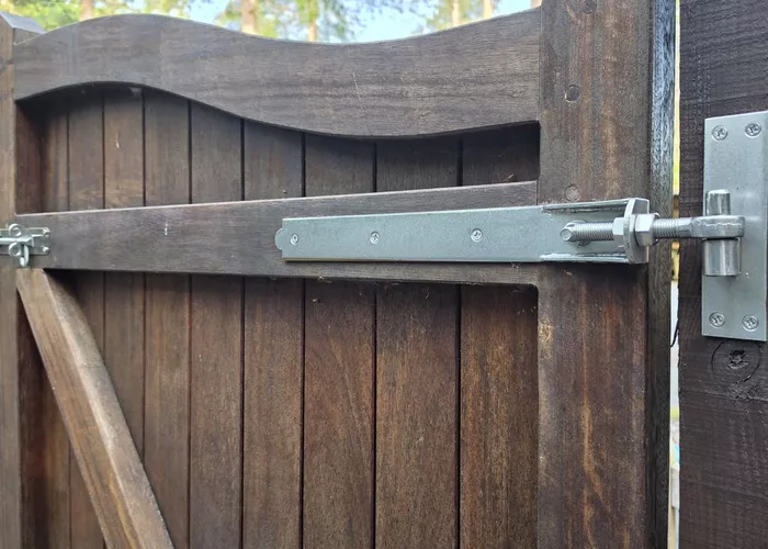 Close-up of a wooden gate latch with metal fittings in a forest setting.