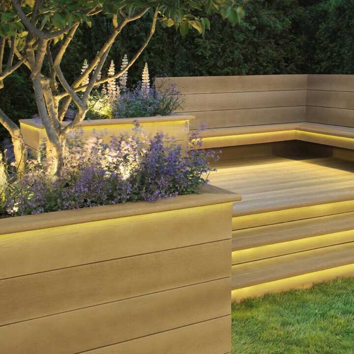 Modern outdoor seating area and decking with illuminated planters and decorative plants.