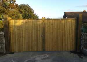 Wooden double gate with a latch, set against a clear sky and greenery.