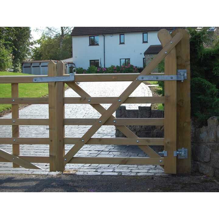 Wooden double gate with metal hinges, set against a gravel pathway and trees.