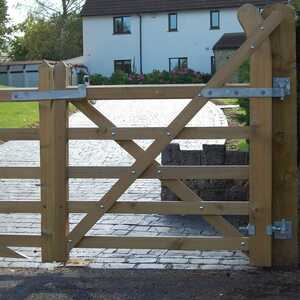Bespoke country-style gate Wooden double gate with metal hinges, set against a gravel pathway and trees.
