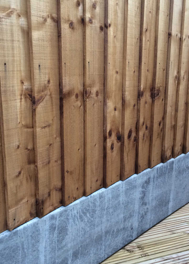 Wooden fence vertical slats with a concrete gravel board and timber decking below.