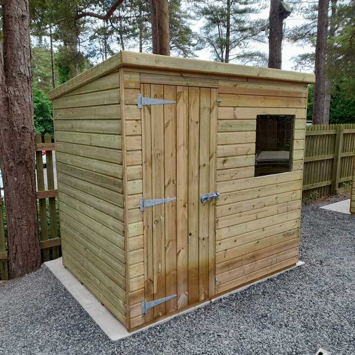 A wooden pent roof shed with a door and a window, surrounded by greenery.