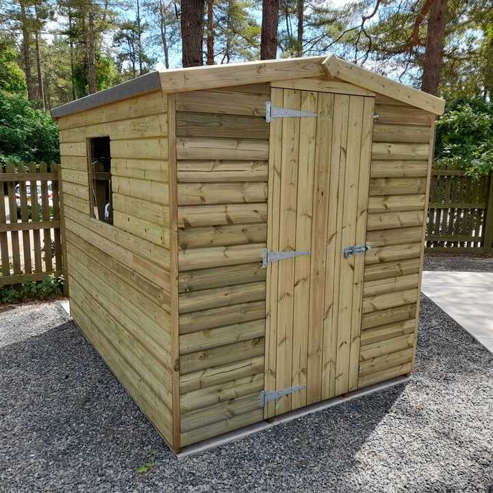 Wooden shed with a door and a window, set on gravel in a wooded area.