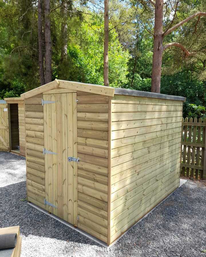 Wooden apex shed surrounded by trees and gravel.