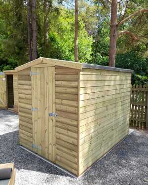 Wooden apex shed surrounded by trees and gravel.