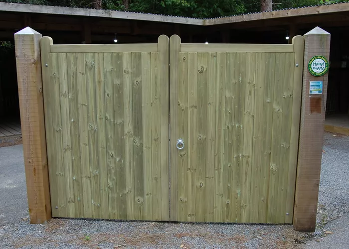 Wooden double gates with a lock, set within a fence, on a gravel pathway.