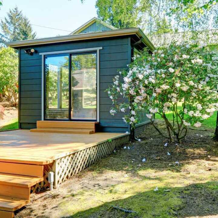 An outdoor office with a wooden deck, surrounded by greenery and a tree.
