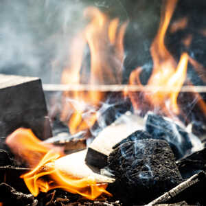 Flames and smoke rising from burning wood and charcoal.
