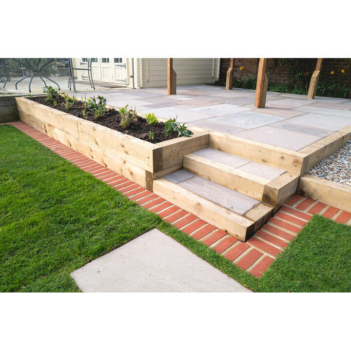 Timber sleepers line steps leading up to a patio with planting boxes and brick borders in a garden setting.