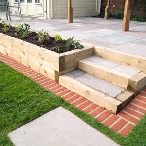 Timber sleepers line steps leading up to a patio with planting boxes and brick borders in a garden setting.