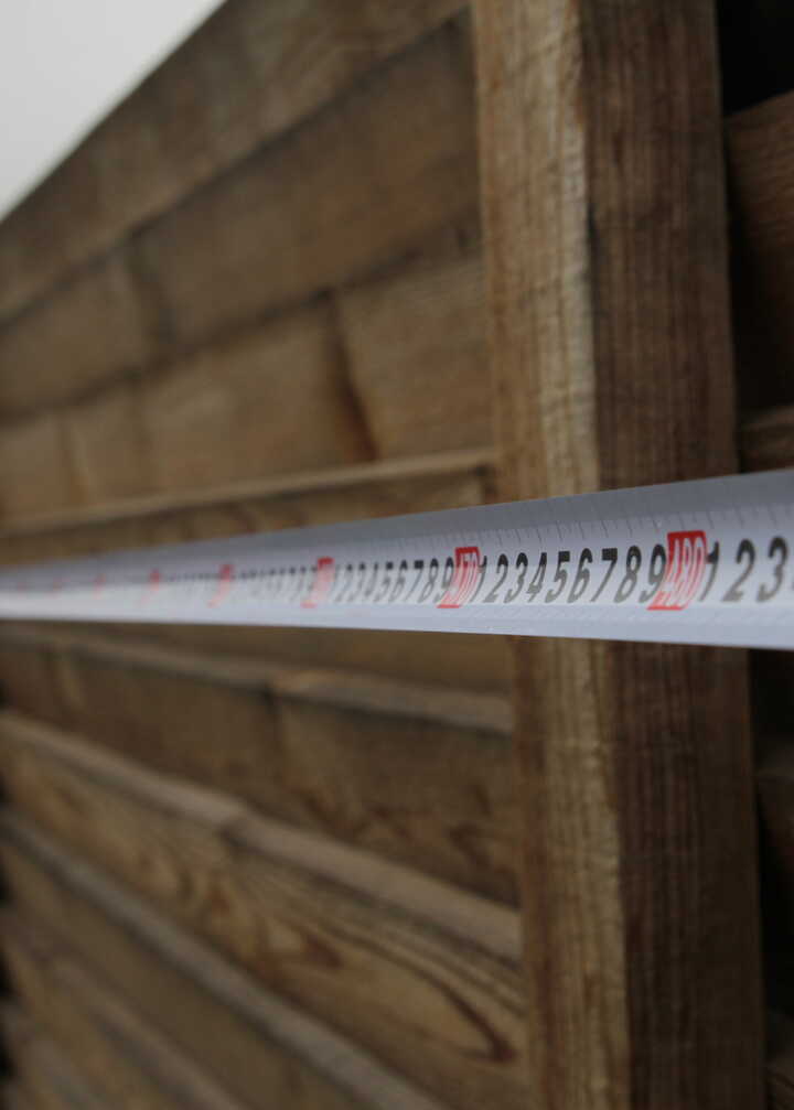 A measuring tape extended along a wooden fence in an outdoor setting.