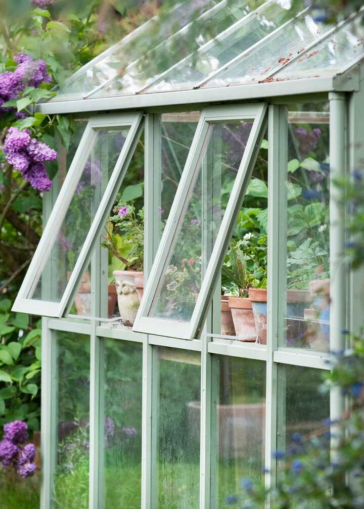 Greenhouse surrounded by blooming flowers in a garden.