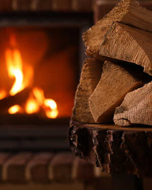 Stack of firewood in front of a glowing fireplace. Warm and cozy ambiance.