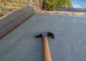 A close-up of a hammer resting on a felted shed roof