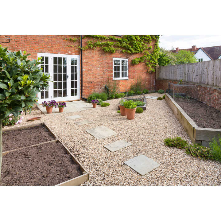 Garden with gravel path, potted plants, and raised sleeper beds against a brick house.