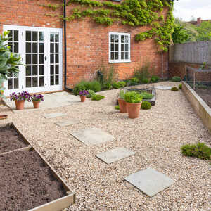 Garden with gravel path, potted plants, and raised sleeper beds against a brick house.