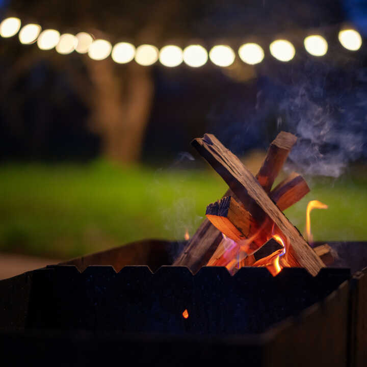 A nighttime campfire with glowing logs and string lights in the background.