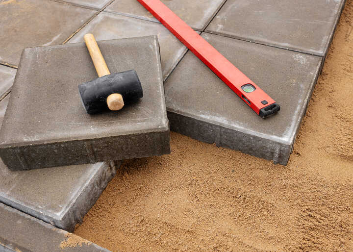 Tools and pavers on sand, including a rubber mallet and level.