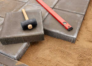 Tools and pavers on sand, including a rubber mallet and level.
