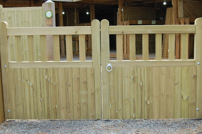 Wooden Banff driveway gate with an arched top, secured with metal latches in a gravel area.