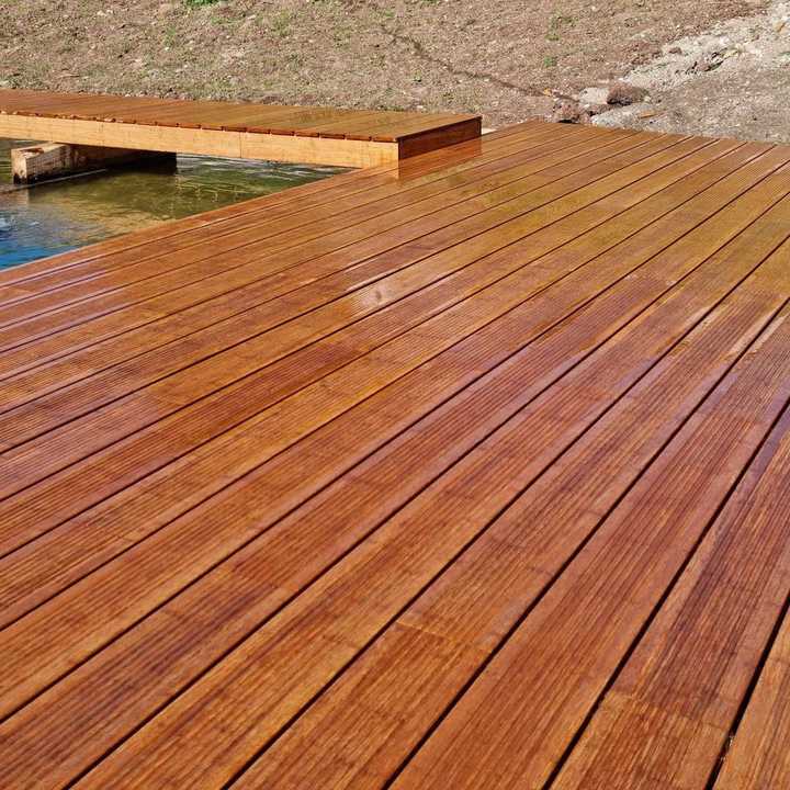 Bamboo decking with smooth planks, extending over water and surrounded by dry grass.