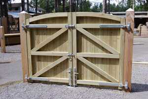 Wooden double gates with an arched top, secured with metal latches in a gravel area.