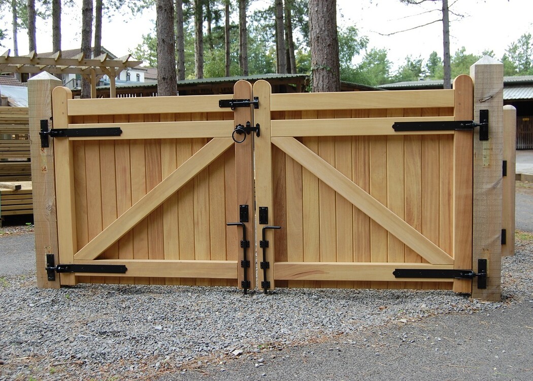 Wooden double gate with metal hinges, set against a gravel pathway and trees.