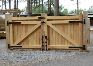 Wooden double gate with metal hinges, set against a gravel pathway and trees.