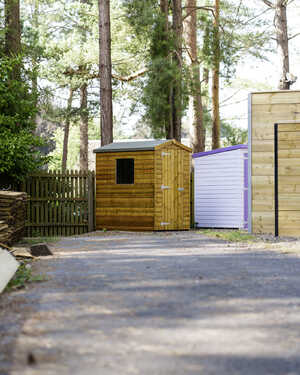 Three small sheds among trees, with a gravel path leading toward them.