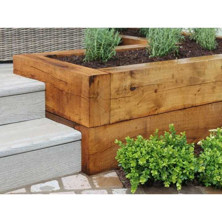 Green oak sleeper raised bed beside stone steps with small green plants nearby.