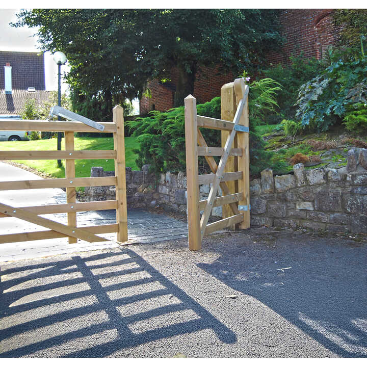 Wooden gate opening onto a path with greenery and stone wall beside it.