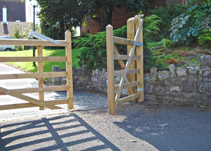 Wooden gate partially opened, leading to a pathway with greenery and a stone wall.