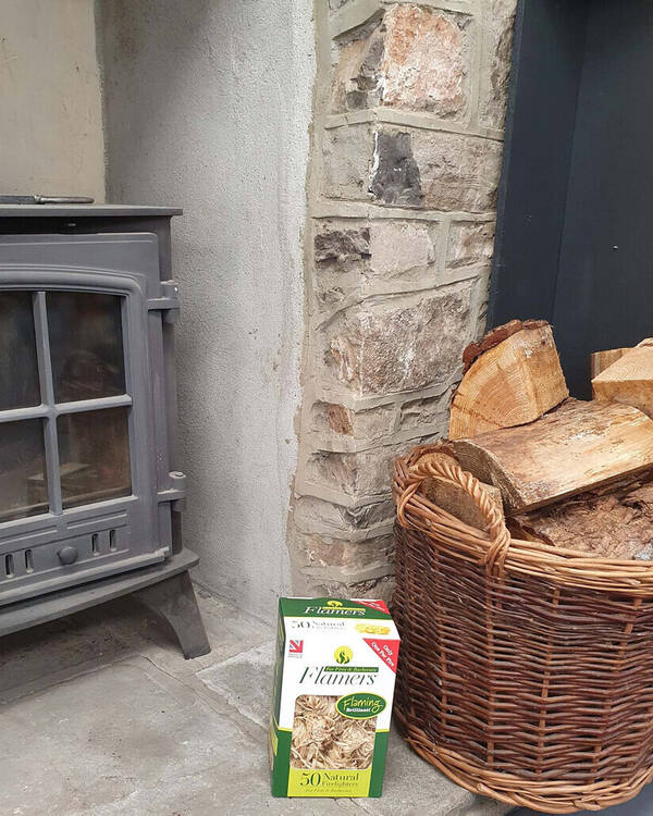 A wood-burning stove next to a basket of firewood and a box of fire starters.