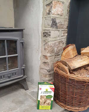 A wood-burning stove next to a basket of firewood and a box of fire starters.