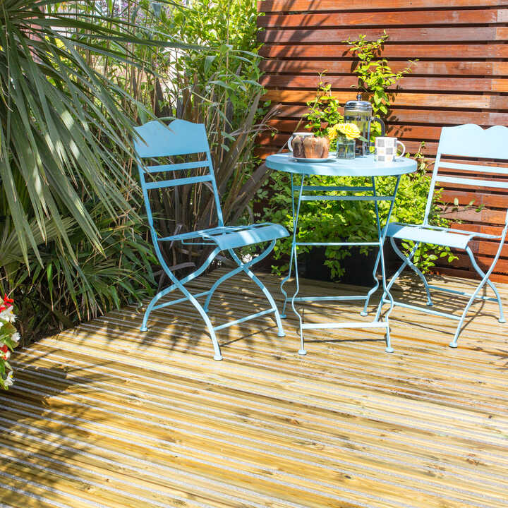 Blue chairs and a table on a timber deck surrounded by plants and flowers.