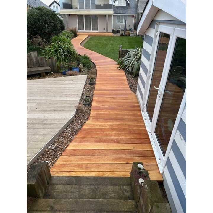 Hardwood decking path winding through a garden, leading to a house with large windows.