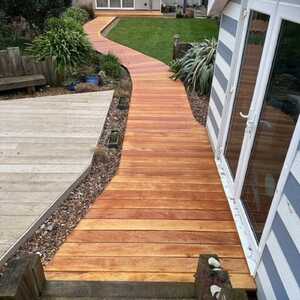 Hardwood decking path winding through a garden, leading to a house with large windows.