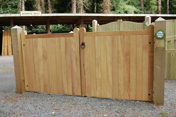 Wooden double gate with a black ring handle, set in a gravel path.