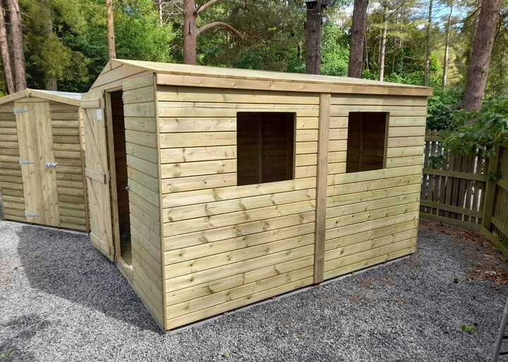 Two wooden Apex sheds with windows, set on gravel in a wooded area.