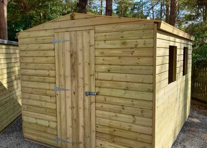 Wooden garden shed with a slanted roof, two windows, and double doors in a gravel area.