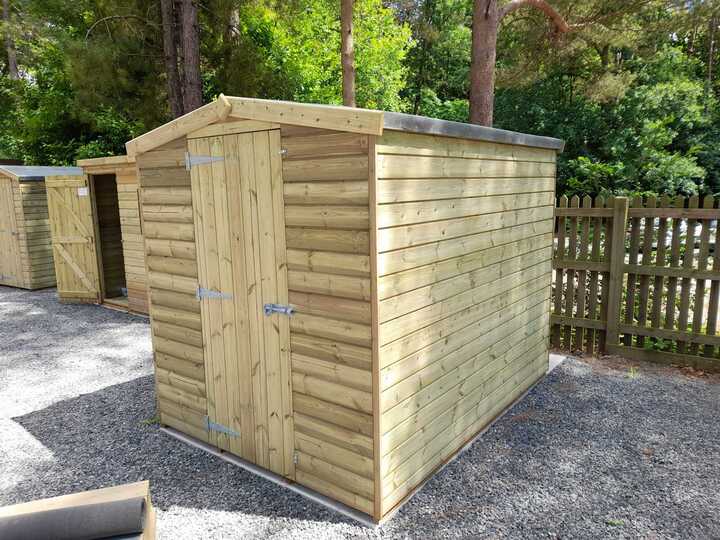 Wooden Apex roof storage shed surrounded by gravel and trees.
