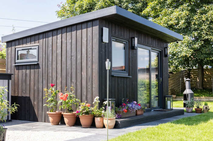 An outdoor office using IRO charcoal cladding surrounded by potted flowers and greenery.