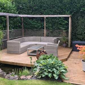 Wooden deck with seating area, greenery, and a small storage shed.