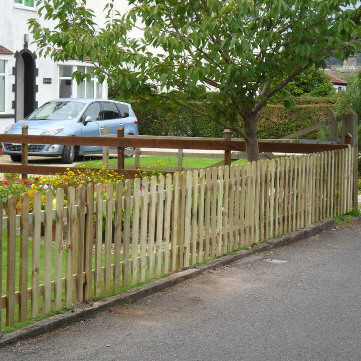 A wooden picket fence runs along a grassy area with a car parked nearby.