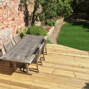 A wooden table and chairs on a wooden deck overlooking a garden with greenery.