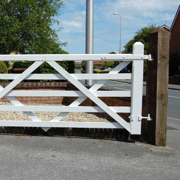 A white wooden gate stands open in front of a house with solar panels on the roof.