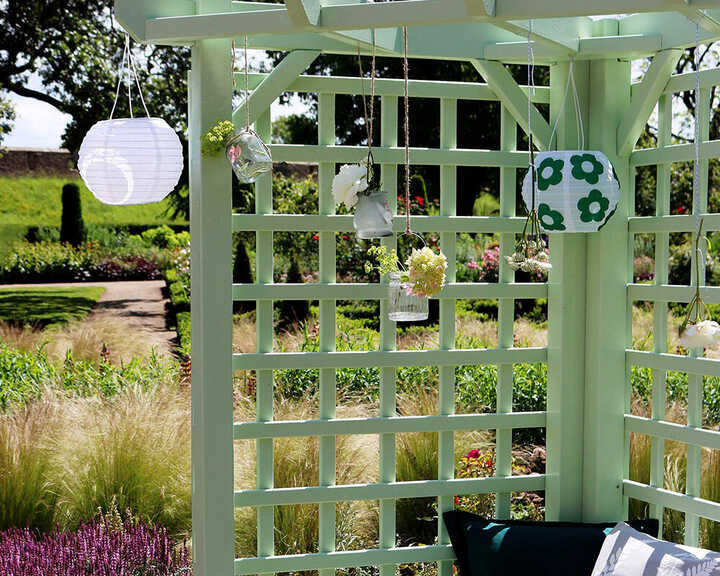 Trellis and arbour painted in Thorndown wood paint decorated with hanging lanterns and flowers in vibrant greenery.