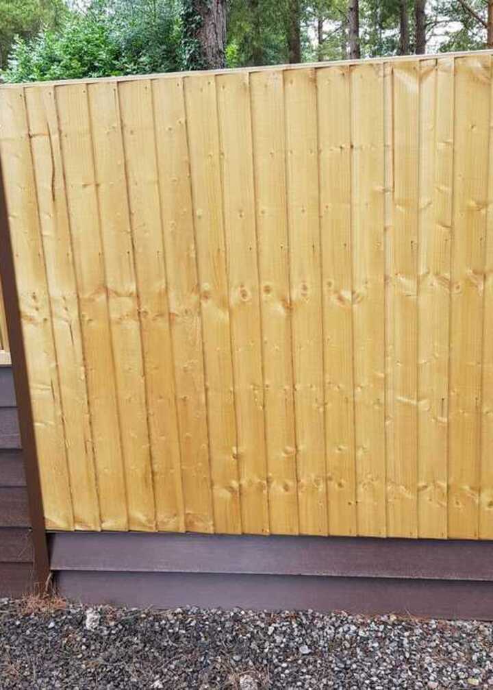 Timber fence panels in natural finish with a brown base, set in a landscaped area.